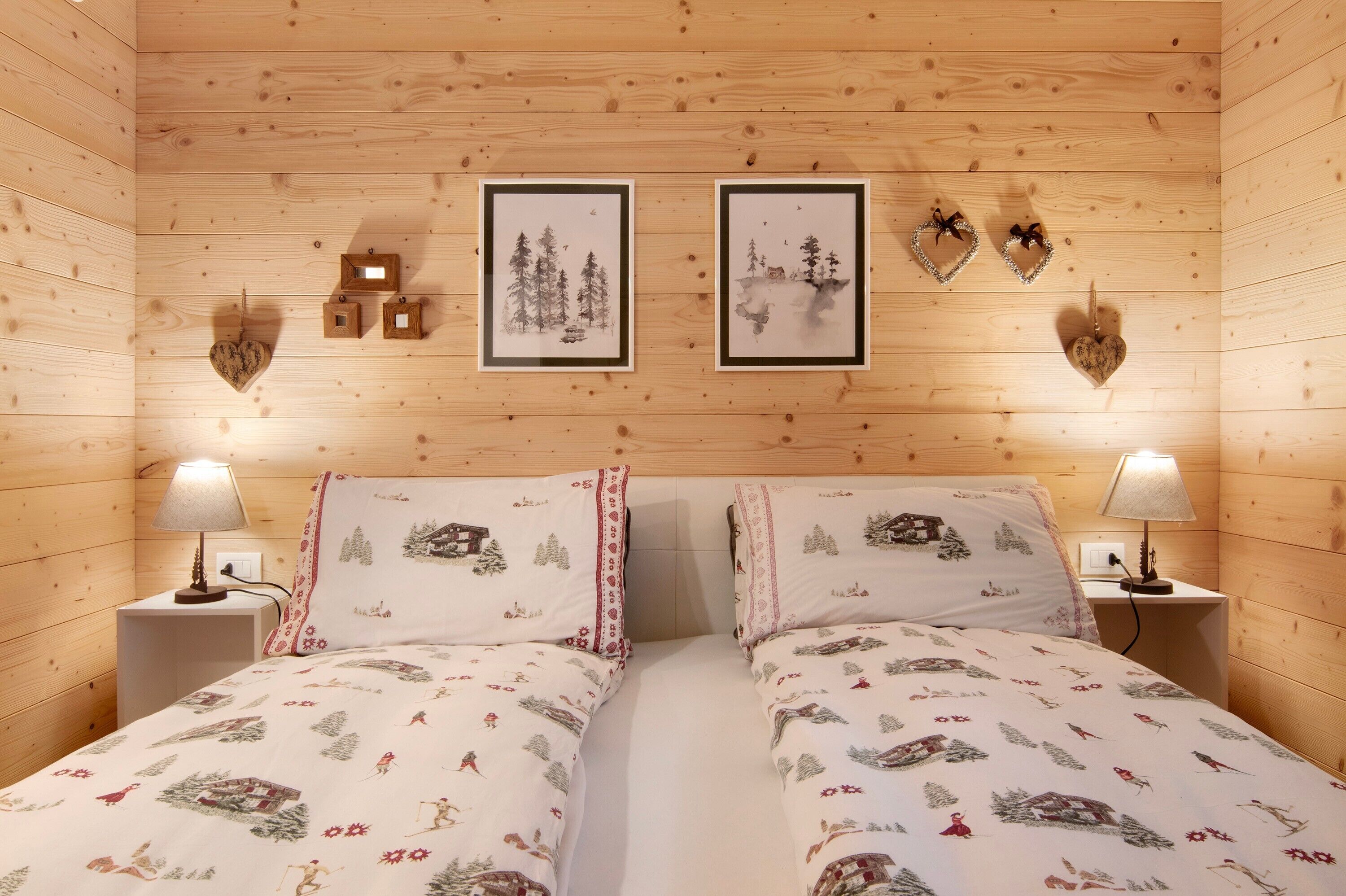A cozy room with wooden walls, two beds with matching bedding, framed pictures on the wall, and bedside lamps.