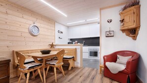 Eine moderne Küche mit Holzschränken, ein Essbereich mit Holztisch und -stühlen, ein rotes Ledersofa und eine an der Wand befestigte Uhr.