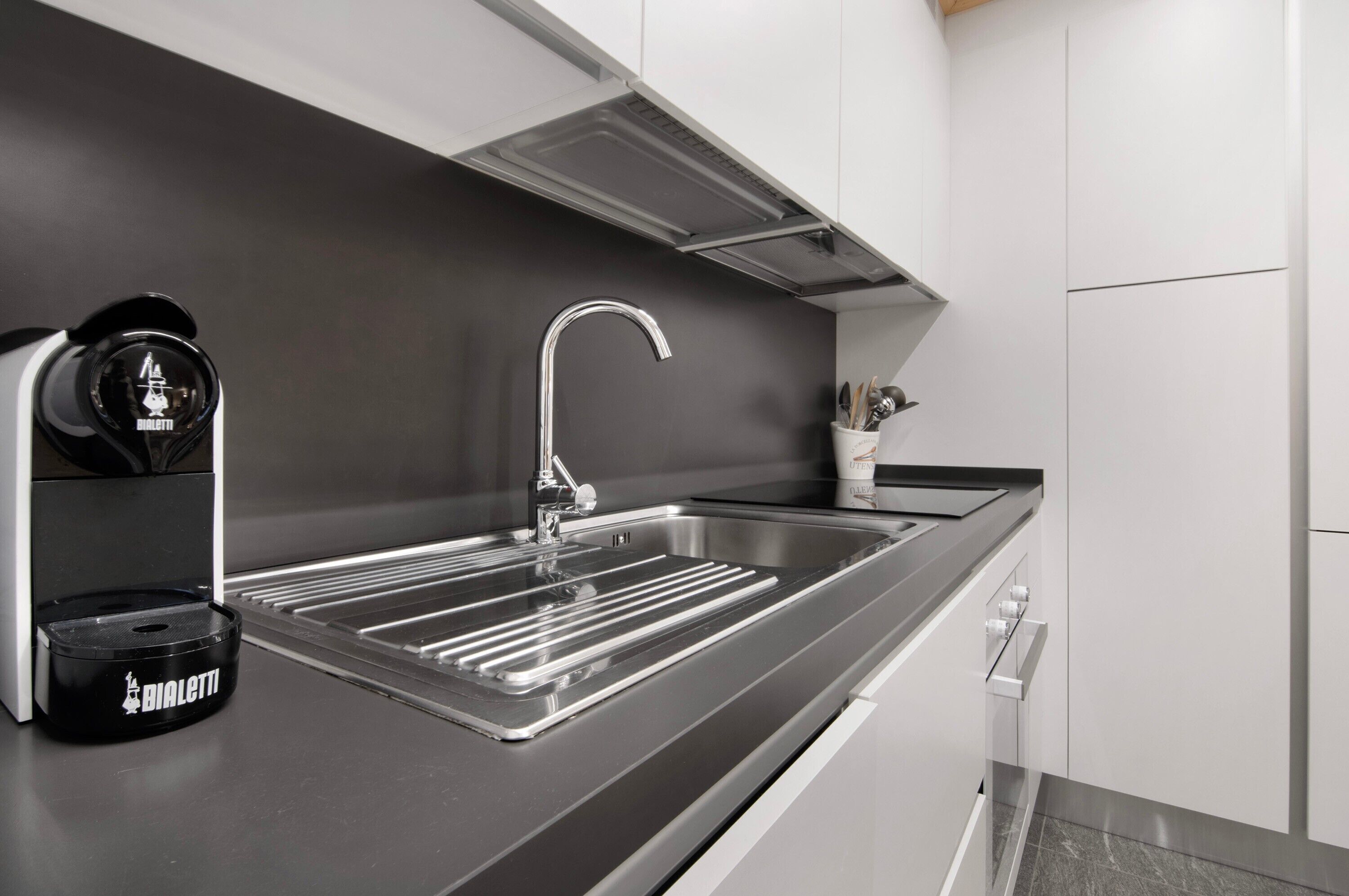 A modern kitchen with a stainless steel sink, a black Bialetti espresso machine, and a sleek countertop.