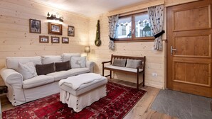 Ein gemütliches Zimmer mit Holzvertäfelung, einer weißen Couch, einer Bank, einem roten Teppich mit Muster und einer Holztür.