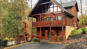 A log cabin with a two-story balcony, surrounded by trees.