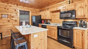 A wooden cabin-style kitchen with a central island, a refrigerator, a microwave, an oven, and a sink.