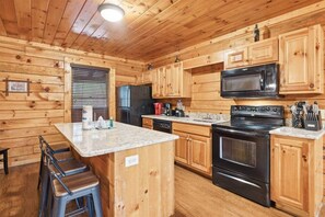 Une cuisine de style rustique, avec des éléments en bois, comprenant un îlot central, un réfrigérateur, un four à micro-ondes, un four traditionnel et un évier.