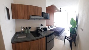 A compact kitchen with a built-in microwave, toaster, and coffee maker. A small dining area with a bench and a potted plant is visible. - Beautiful & Fully Equipped Condo Studio Strategically located (Tulum)