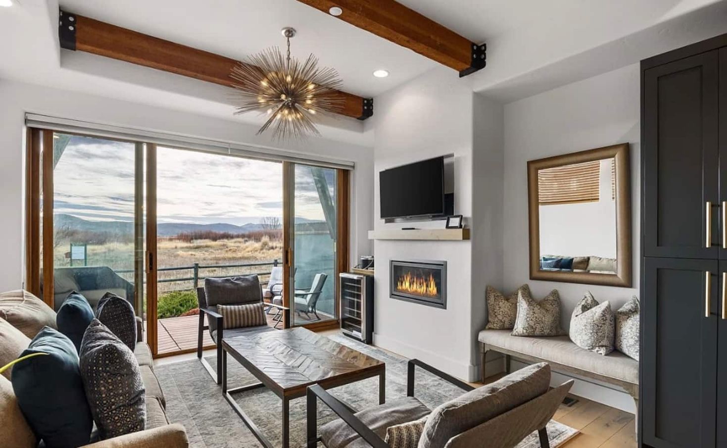 A modern living room with a fireplace, a television, and a large window overlooking a landscape.