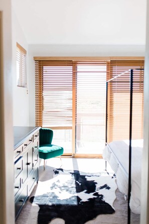Un dormitorio con cama, una silla, un aparador y una ventana con persianas.