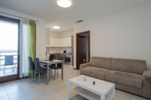 Una sala de estar moderna con un sofá, una mesa de comedor con sillas, una cocina al fondo y un balcón con vistas.