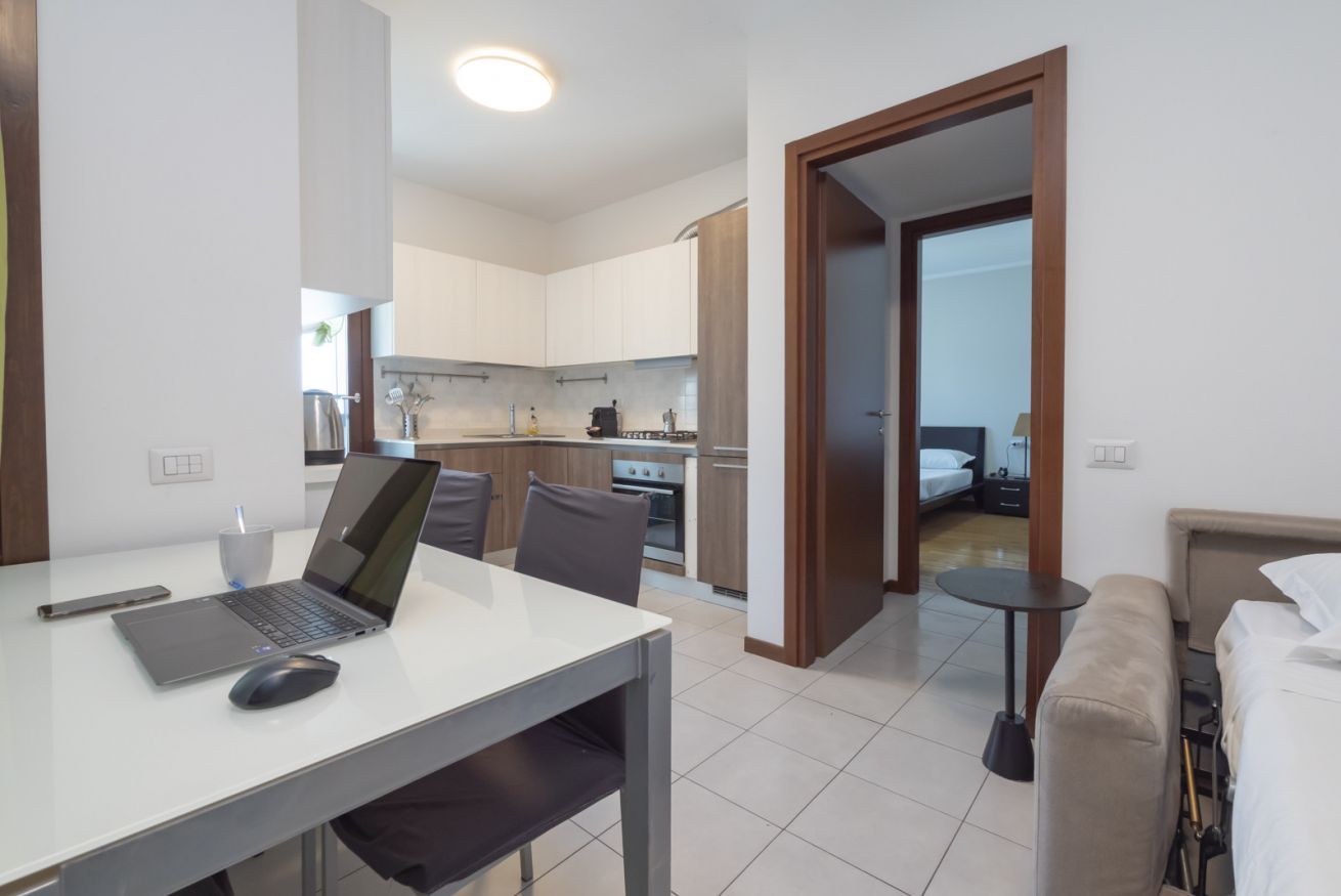 A modern hotel room with a kitchenette, a dining area with a laptop, and a bed.