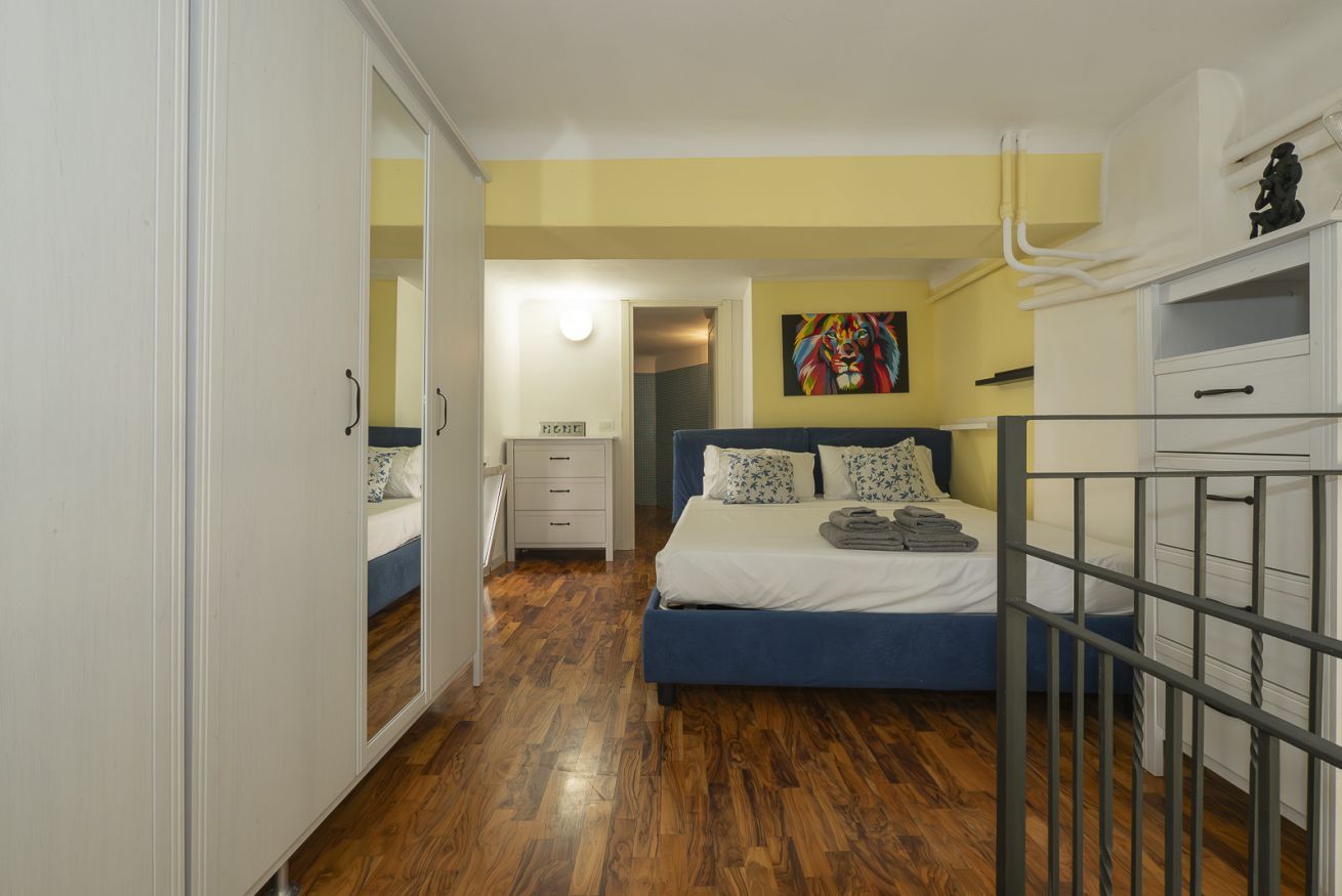 A bedroom with a bed, a wardrobe, a nightstand, and a painting on the wall.