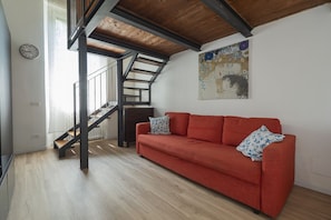 A modern living room with a wooden staircase, a red sofa, and a large abstract painting on the wall.