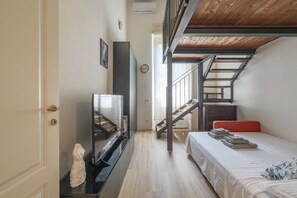 A room with a bed, a TV, a statue, a staircase, and a window.