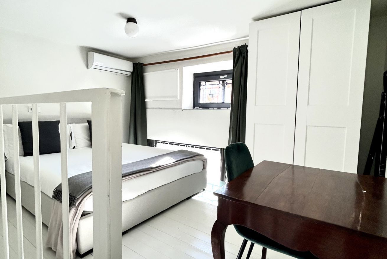 A bedroom with a bed, a wooden table, a chair, a wardrobe, and a window with curtains.