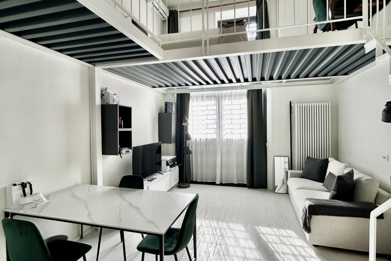 Et moderne, kompakt opholdsrum med spiseplads, sofa og trappe op til en etage over.