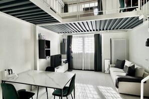 A modern, compact living space with a dining area, sofa, and a staircase leading to an upper level.