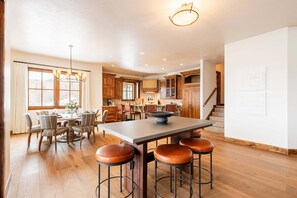Une cuisine spacieuse avec des meubles de rangement en bois, un coin repas doté d’une grande table et de chaises, et un escalier menant à un autre niveau.