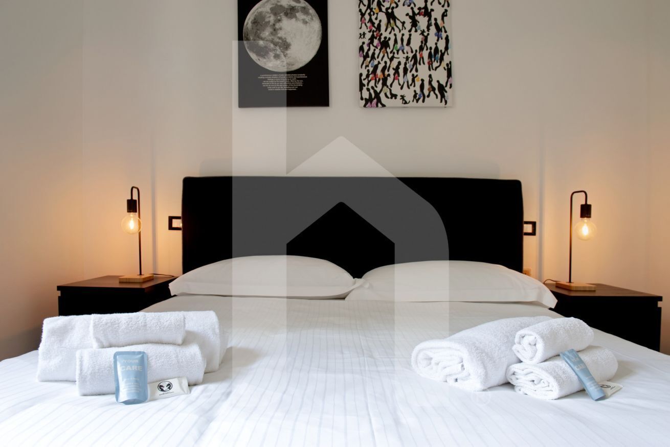 A hotel room with a large bed, two bedside tables, and a nightstand. There are towels and toiletries on the bed.