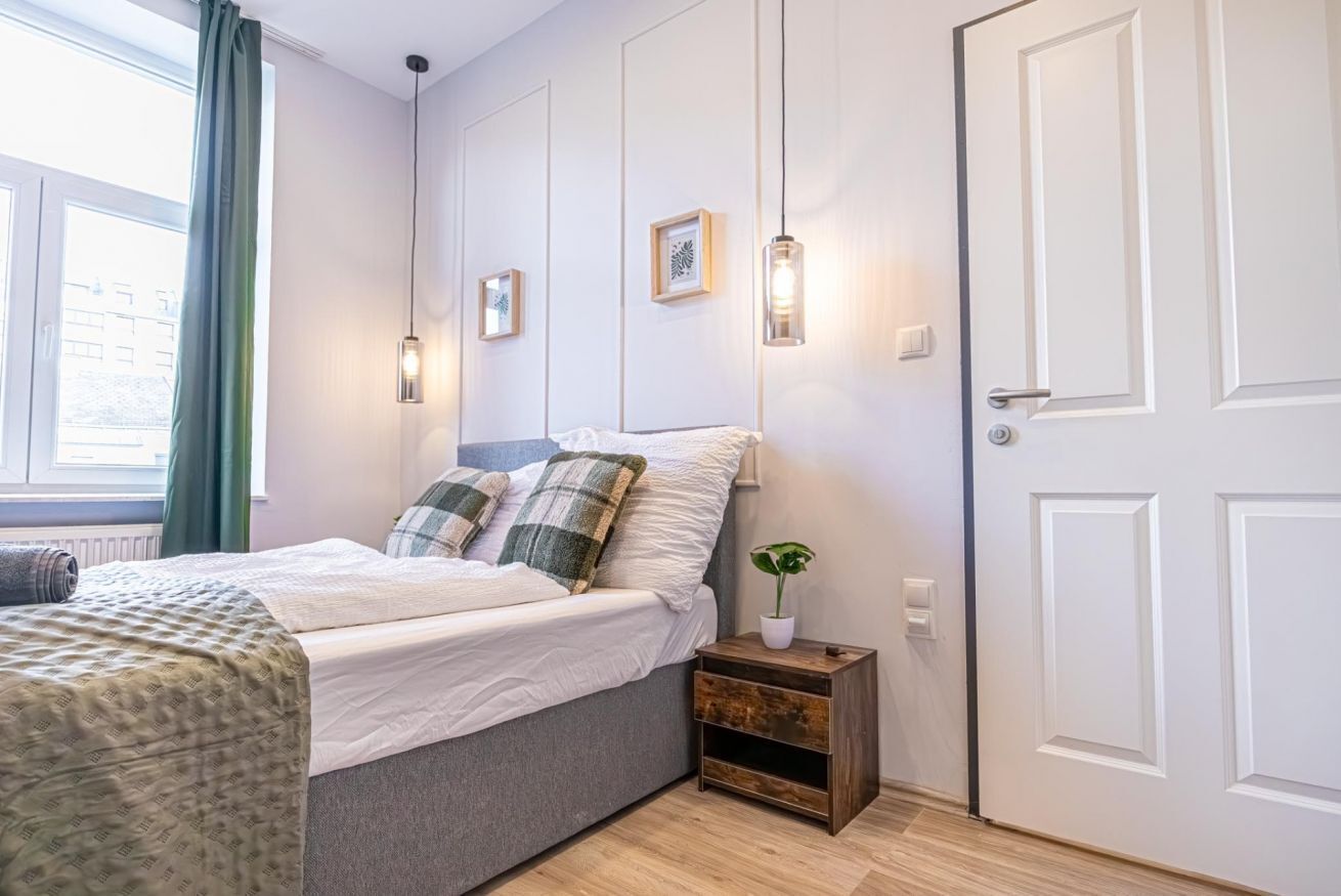 Une chambre à coucher comprenant un lit, une table de chevet, des lampes fixées au mur et une fenêtre avec des rideaux.