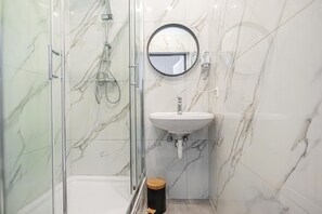 Un baño con ducha envuelta en vidrio, un lavabo blanco y una pared de mármol.