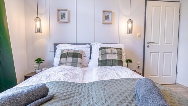 A neatly made bed with a white and green checkered blanket, two bedside tables with small plants, and a white door. - Bright & Modern Room in Vienna’s Meidling District (Vienna)