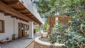 Un bâtiment moderne doté d’un mur en pierre, de poutres en bois et d’un petit jardin agrémenté d’un arbre et de plantes en pot.