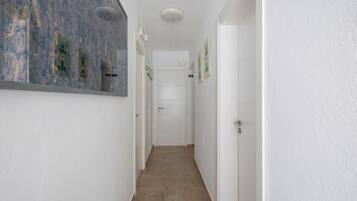 Un couloir étroit aux murs blancs, doté d’un sol carrelé et d’une porte au fond.