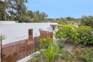 A white building with a wooden door and window shutters, surrounded by a bamboo fence and various plants. - Room 'Doble - 1' with Mountain View, Wi-Fi and Air Conditioning (Santa Eulària des Riu)