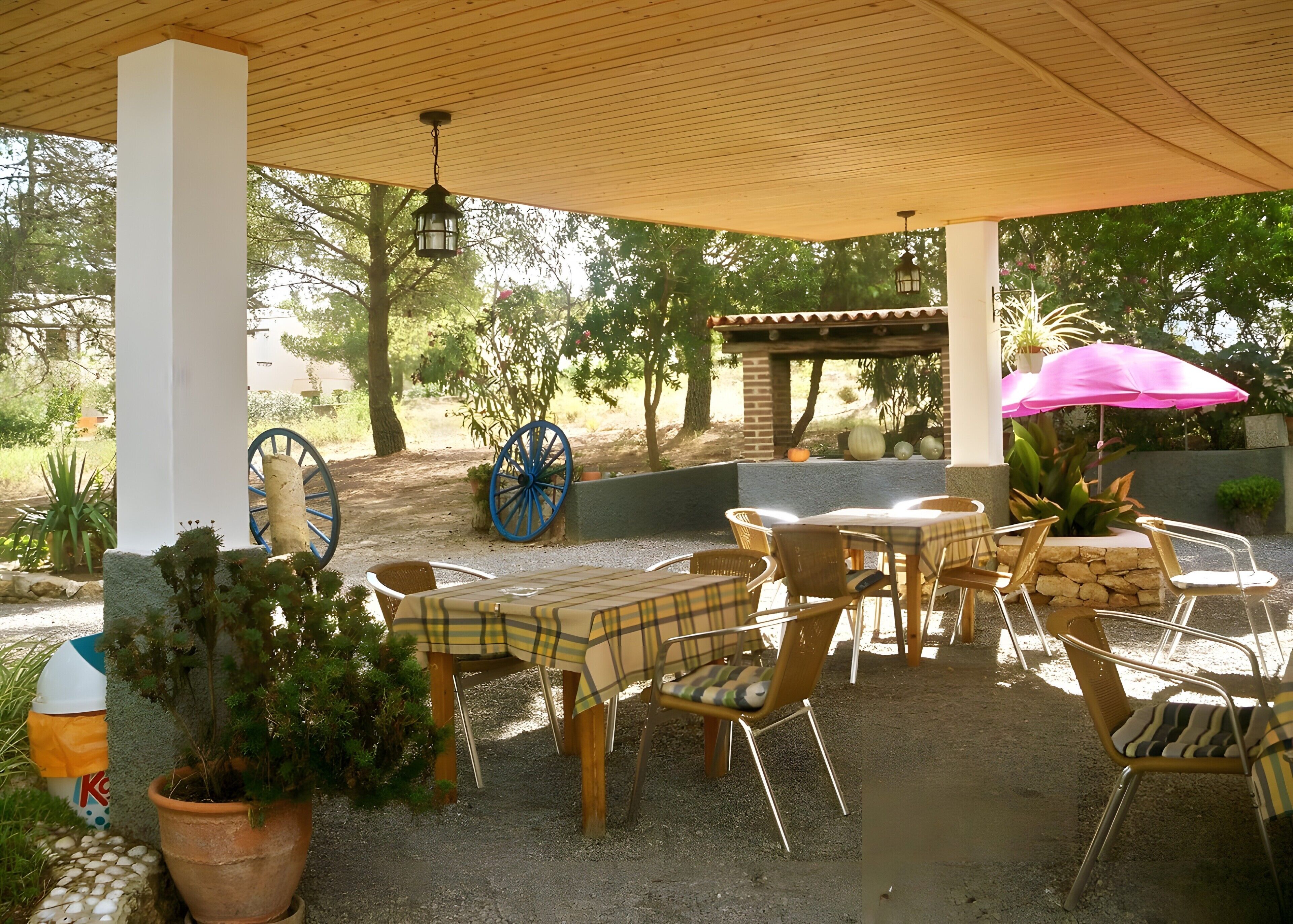 An outdoor patio with tables and chairs, a wooden ceiling, and potted plants.