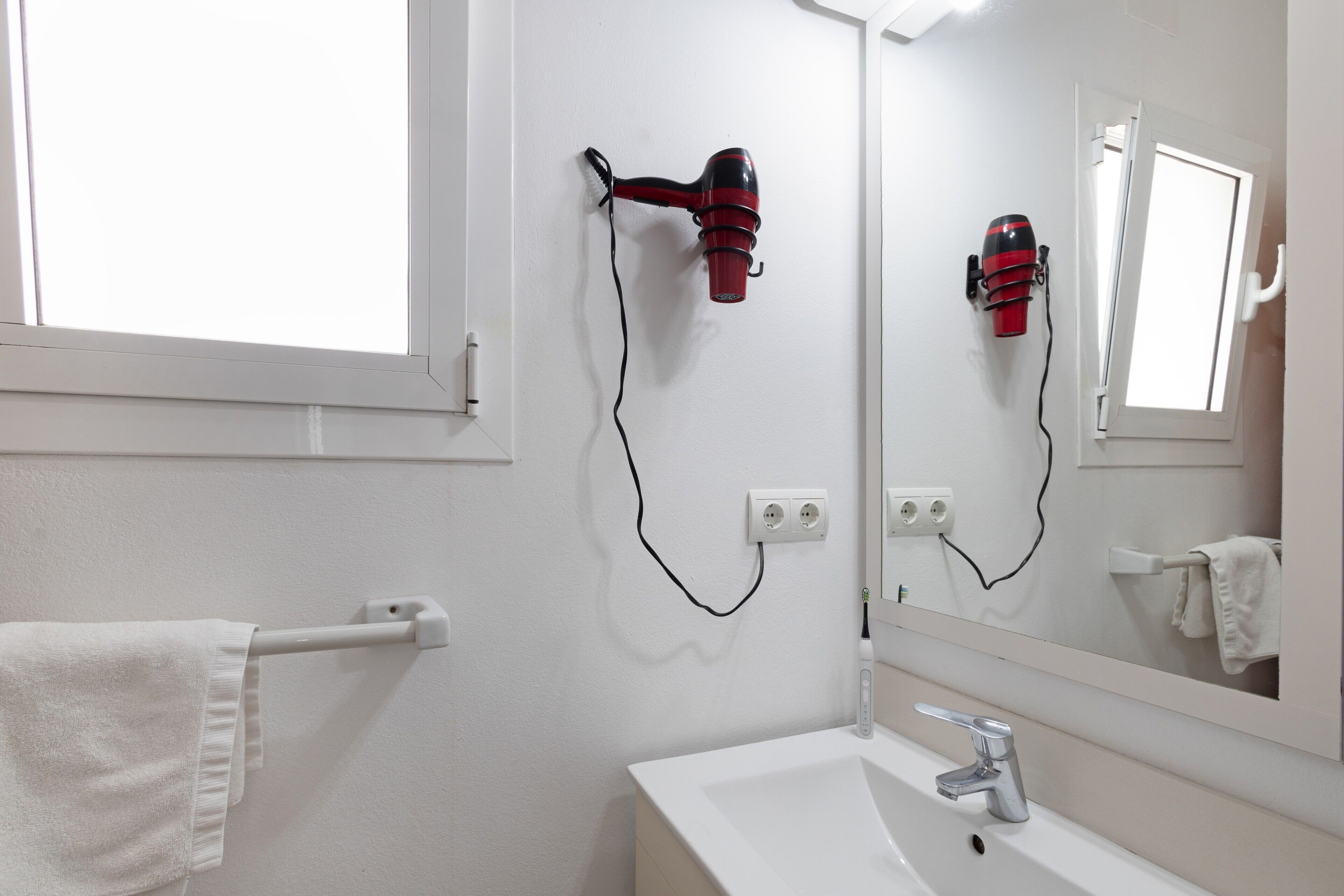 A bathroom with a white sink, a mirror, a towel rack, and a hairdryer mounted on the wall.