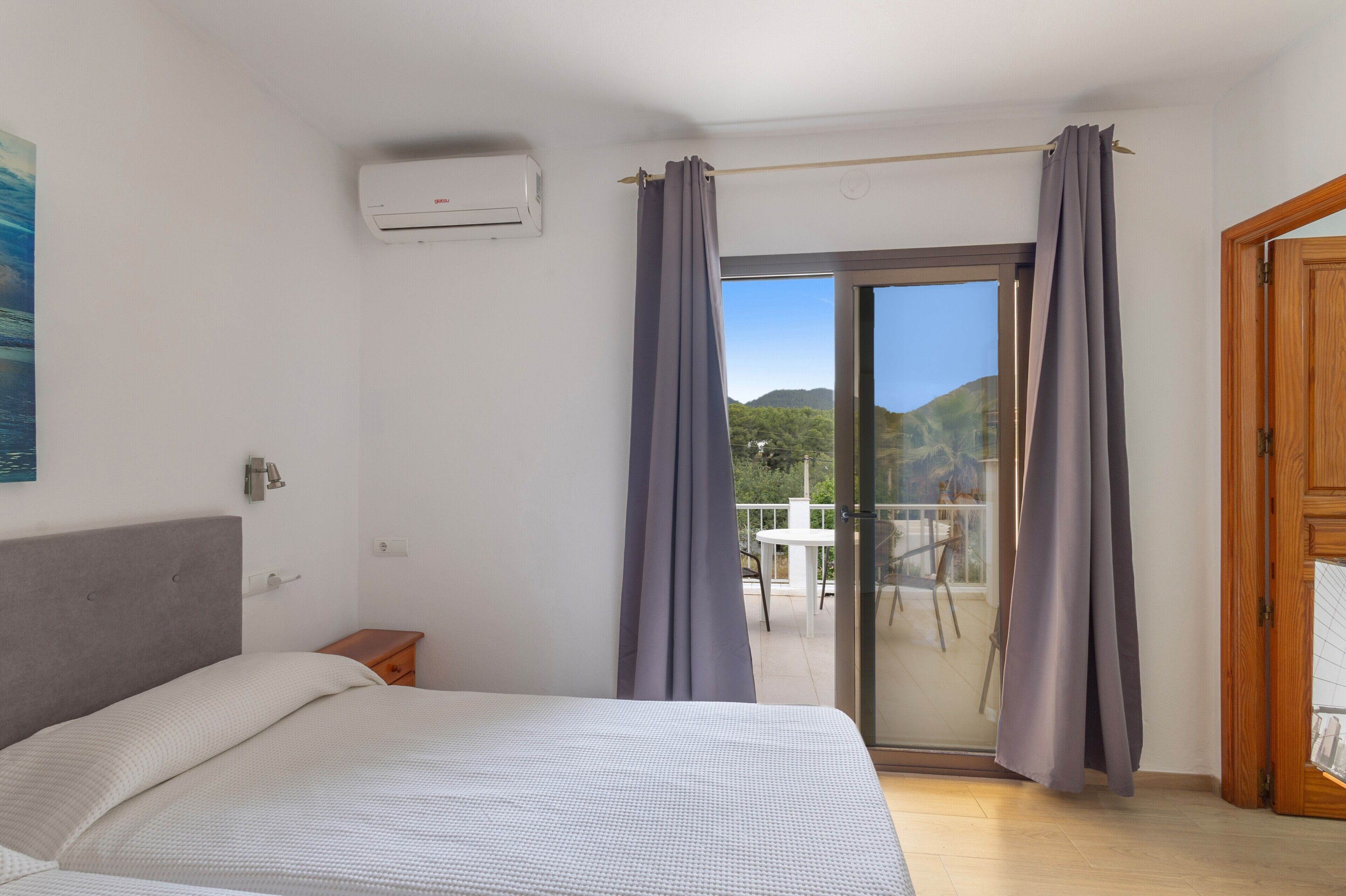 Ein Schlafzimmer mit Bett, Klimaanlage, einer Glasschiebetür zum Balkon und einer Holztür.