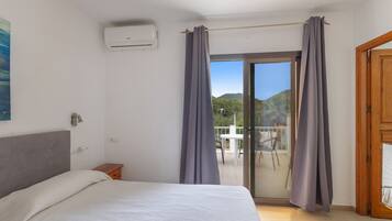 Ein Schlafzimmer mit Bett, Klimaanlage, einer Glasschiebetür zum Balkon und einer Holztür.