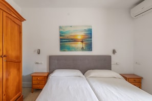 A bedroom with a bed, two bedside tables, a wooden wardrobe, and a painting of a sunset on the wall. - Room 'Doble - 2' with Mountain View, Wi-Fi and Air Conditioning (Santa Eulària des Riu)