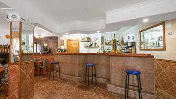 Una zona de bar con mostrador, taburetes y estanterías llenas de botellas.
