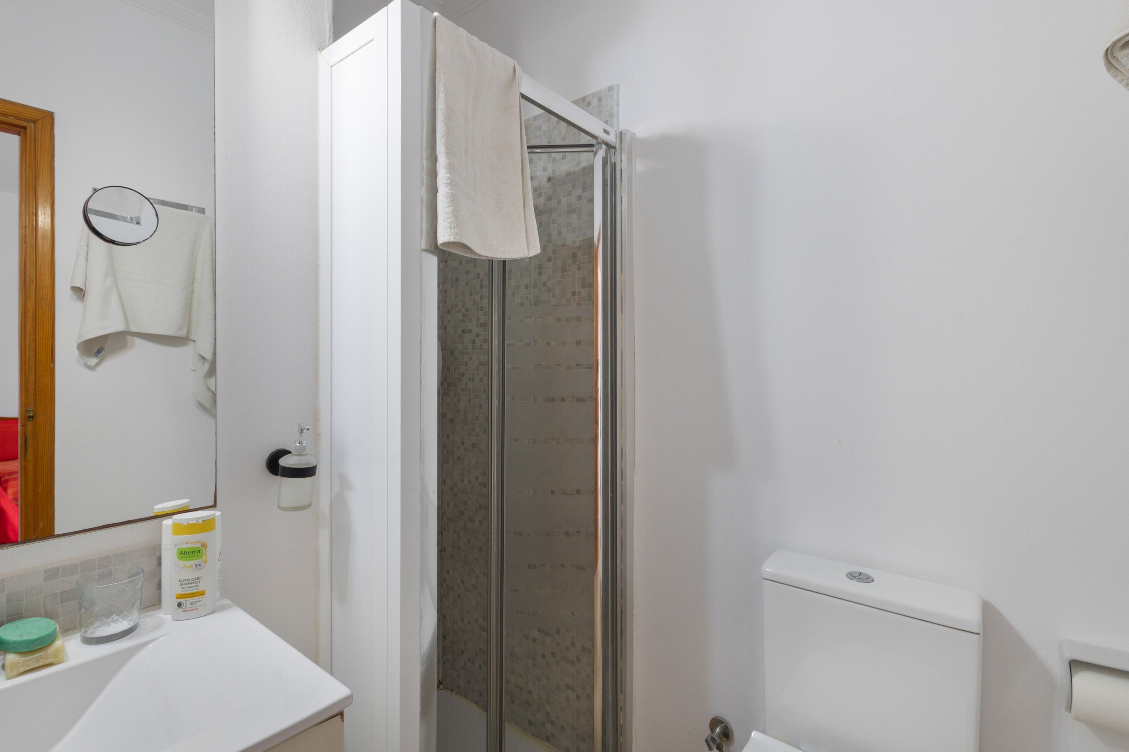 Une salle de bain équipée d’une douche, de toilettes, d’un lavabo et d’un miroir auquel est accrochée une serviette.