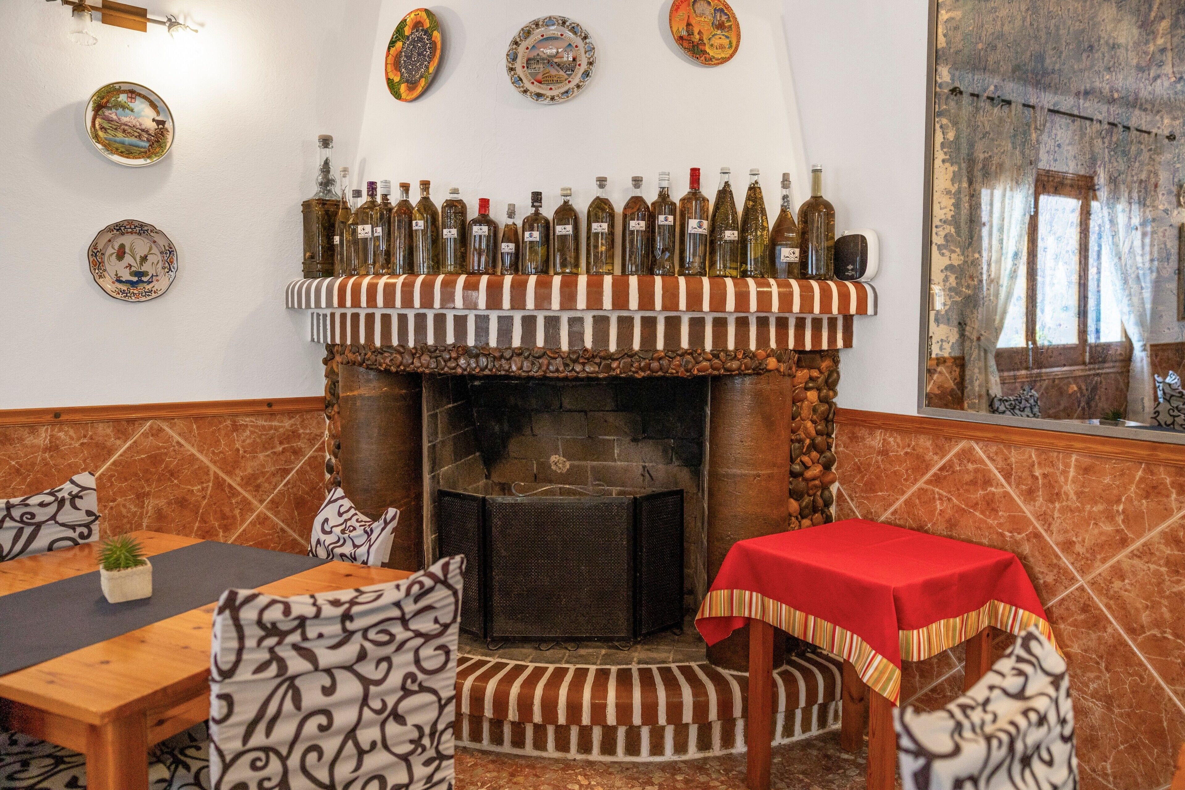 A restaurant interior with a brick fireplace, a long bar with bottles, and a dining area with a red tablecloth.