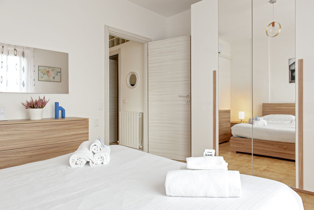 A hotel room with a bed, a bedside table, a mirror, a wardrobe, and a bathroom visible through an open door.