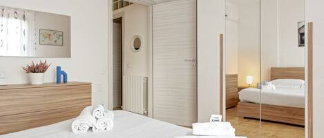 A hotel room with a bed, a bedside table, a mirror, a wardrobe, and a bathroom visible through an open door.