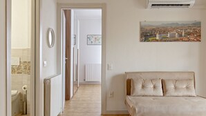 A living room with a beige sofa, a radiator, and a wall-mounted air conditioner. - Homiday - Hospital/Airport- A/C and Free Parking (Pisa)