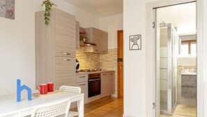 A modern kitchen with a white table and chairs, a wooden cabinet, and a red plant. - Homiday - Hospital/Airport- A/C and Free Parking (Pisa)