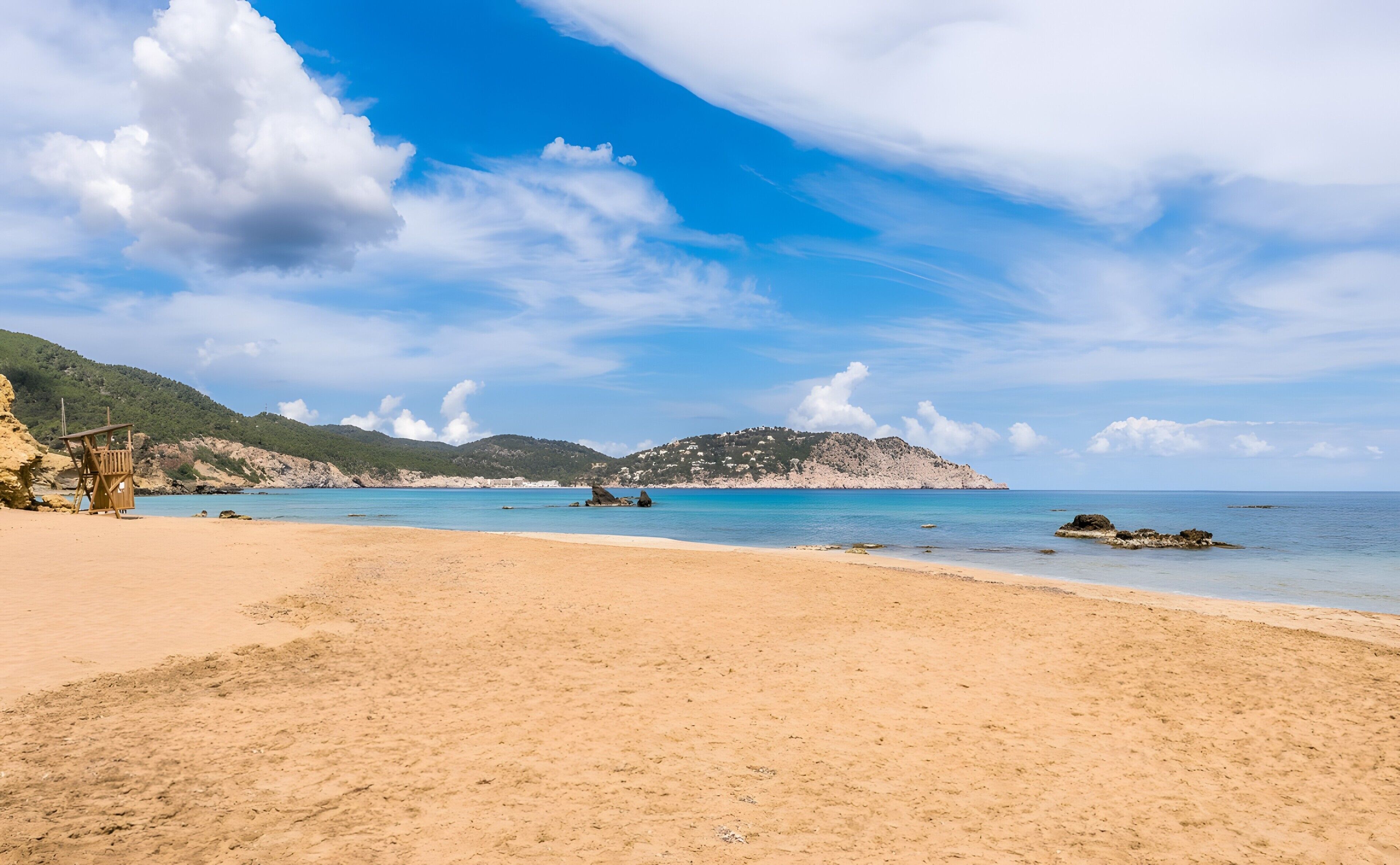 Una playa con cielos despejados, una torre de salvavidas y terreno rocoso.