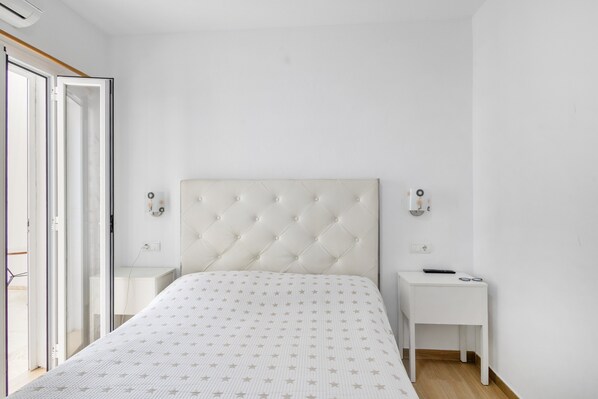 A bedroom with a tufted headboard, a bedside table with a remote control, and a small bedside table with glasses. - Room 'Doble - 4' with Mountain View, Wi-Fi and Air Conditioning (Santa Eulària des Riu)