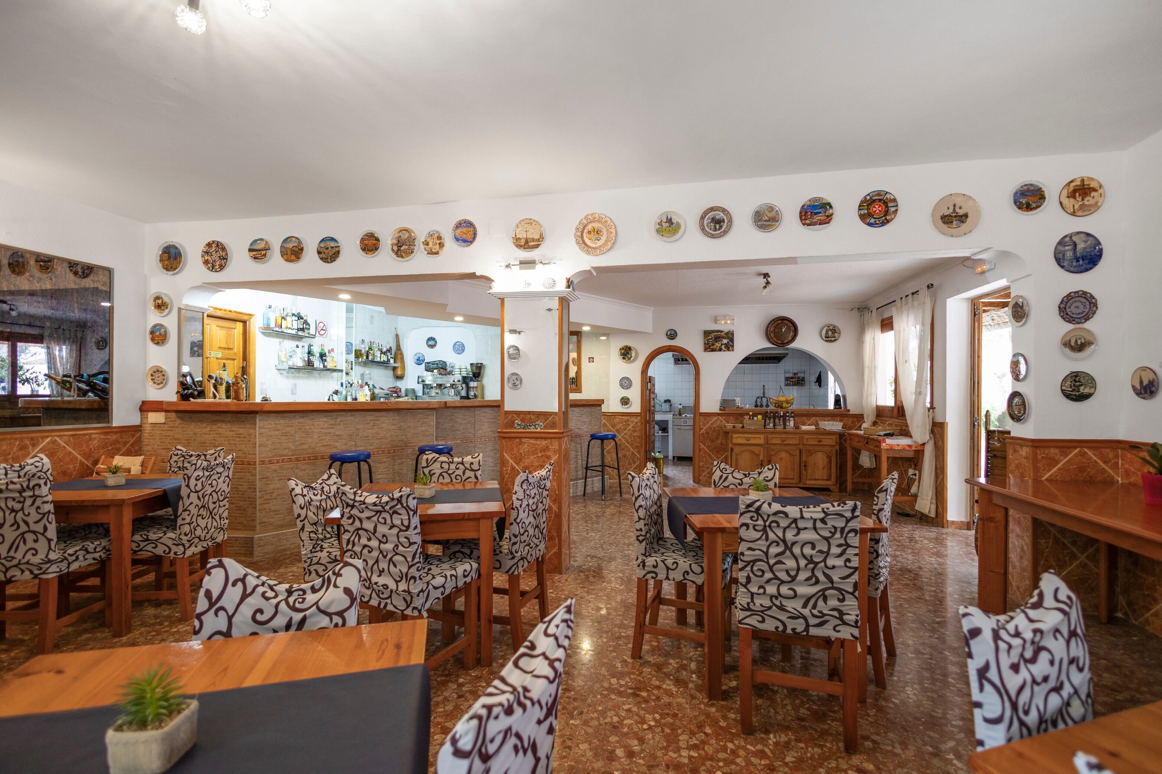 Un restaurante con sillas estampadas, una zona de bar y una cocina visible a través de un arco.