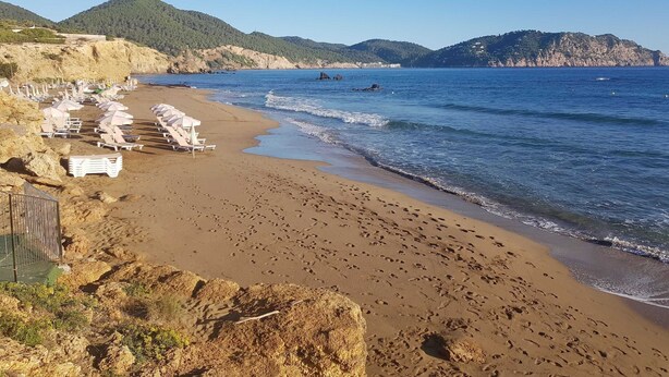 Une plage avec des chaises longues et une falaise rocheuse.