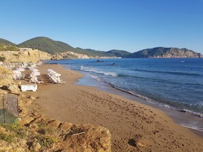 A beach with sun loungers and a rocky cliff. - Room 'Doble - 4' with Mountain View, Wi-Fi and Air Conditioning (Santa Eulària des Riu)