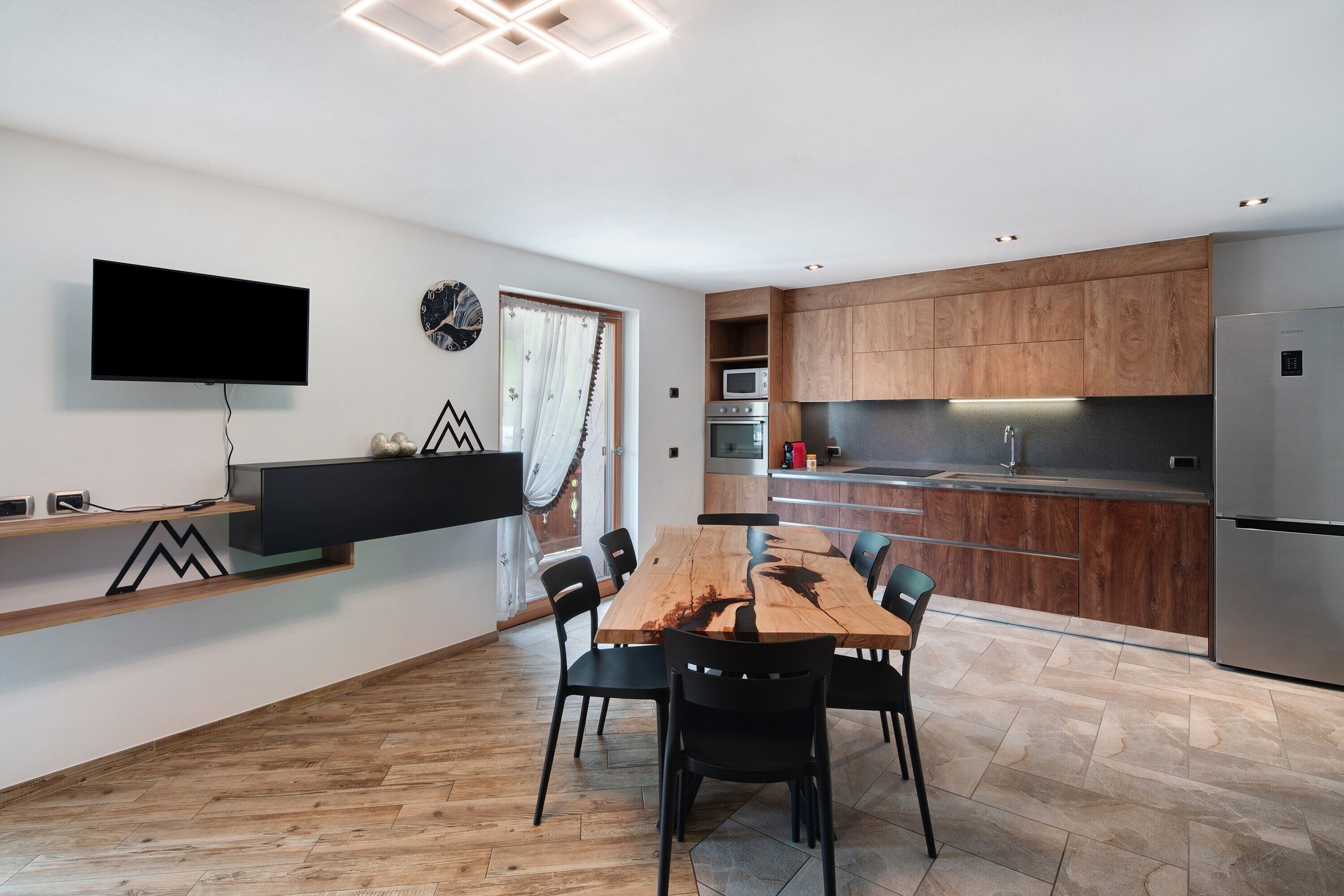 A modern kitchen with wooden cabinets, a built-in oven, and a stainless steel refrigerator.