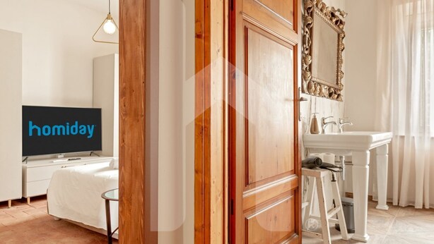 A hotel room with a wooden wardrobe, a television, a white dresser, a sink, and a mirror.