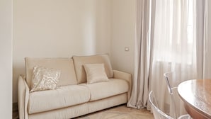 A minimalist living room with a beige sofa, two cushions, and a clear glass table. - RINOCERONTE: Relax and enjoy this simple yet elegant apartment, equipped with all the comforts: PRIVATE parking, FULL HD TV, AIR CONDITIONING, and a fully equipped bathroom with a walk-in shower. All of this just 10 minutes from Pisa and 25 minutes from  (San Giuliano Terme)
