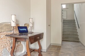 A room with a wooden desk, a laptop, and two lamps. A staircase is visible in the background.