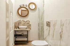 A bathroom with a white sink, a round mirror, a shower with a glass door, and a toilet.