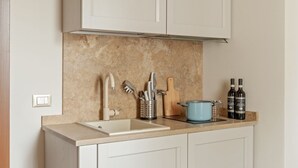 Una cocina con encimera color beige, armarios blancos, pileta doble, una olla azul y dos botellas de vino.