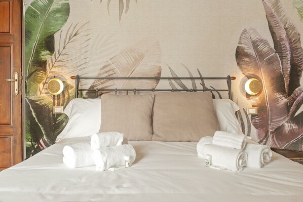 A hotel room with a bed, two bedside lamps, and a tropical leaf mural on the wall.
